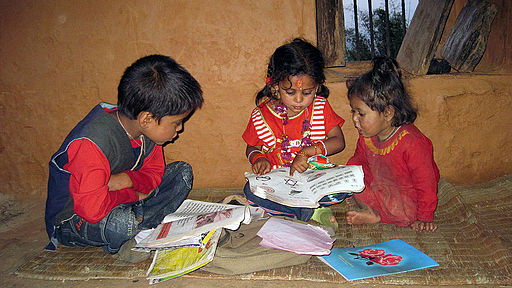 Three children seated on a mat on the floor reading books together.